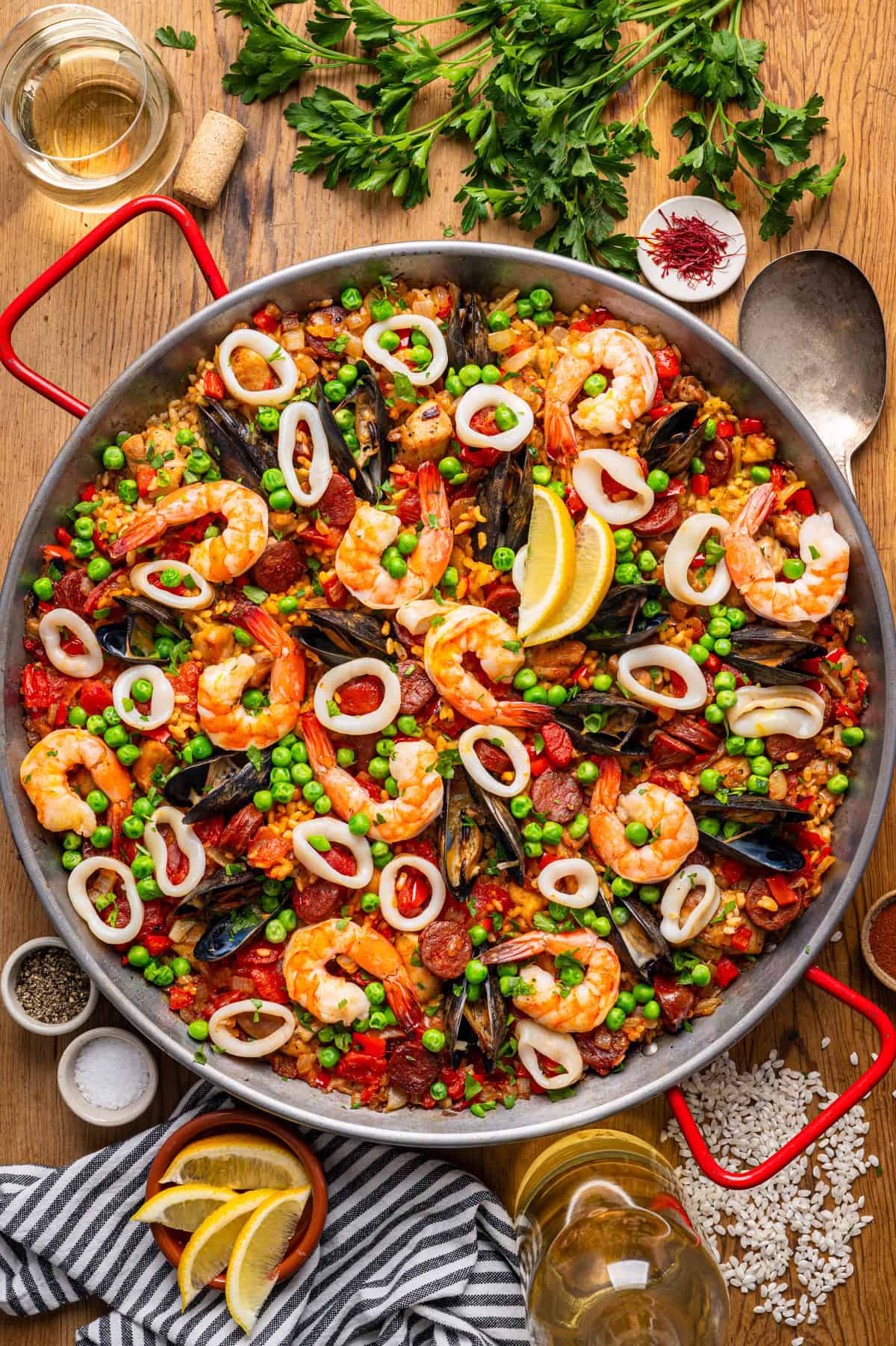 Paella A colorful seafood paella with shrimp, mussels, squid rings, peas, red peppers, and lemon wedges.