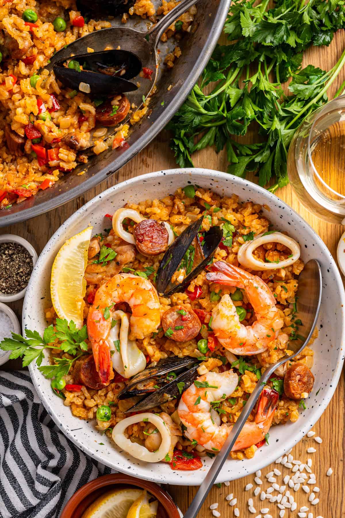 Paella A bowl of seafood paella featuring shrimp, mussels, chorizo, squid rings, peas, and a lemon wedge.