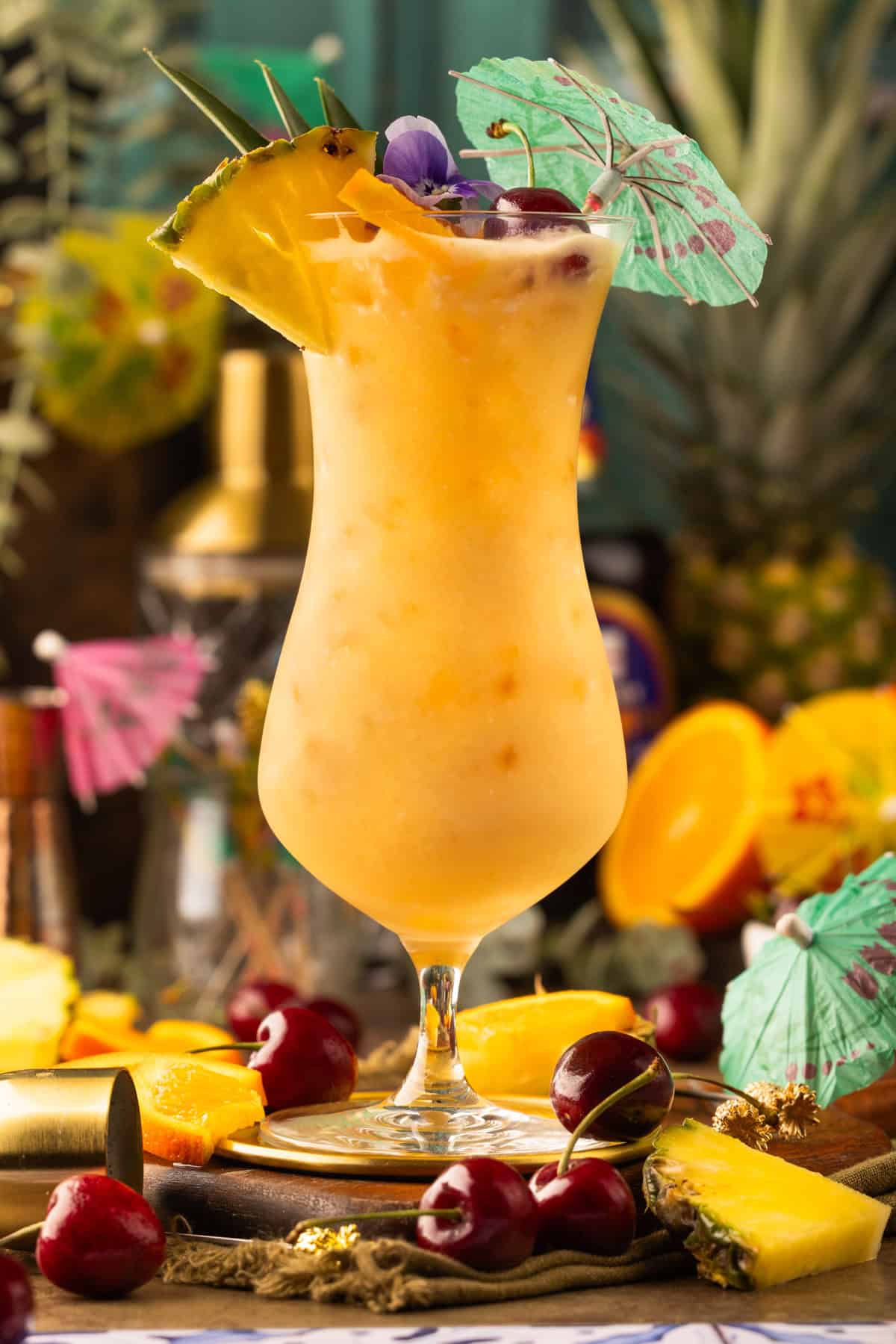 Painkiller Cocktail A tropical cocktail in a curvy glass, garnished with a pineapple slice, cherries, a paper umbrella, and flowers.