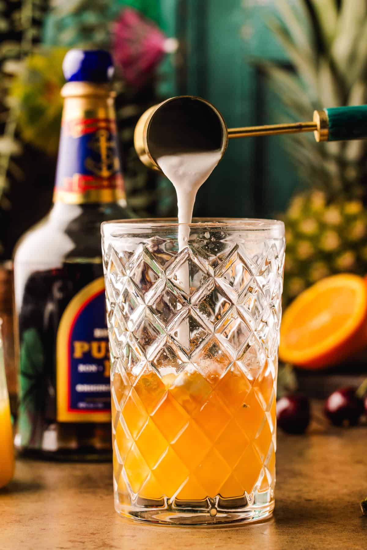 Painkiller Cocktail A metal jigger pours creamy liquid into a glass of orange juice.