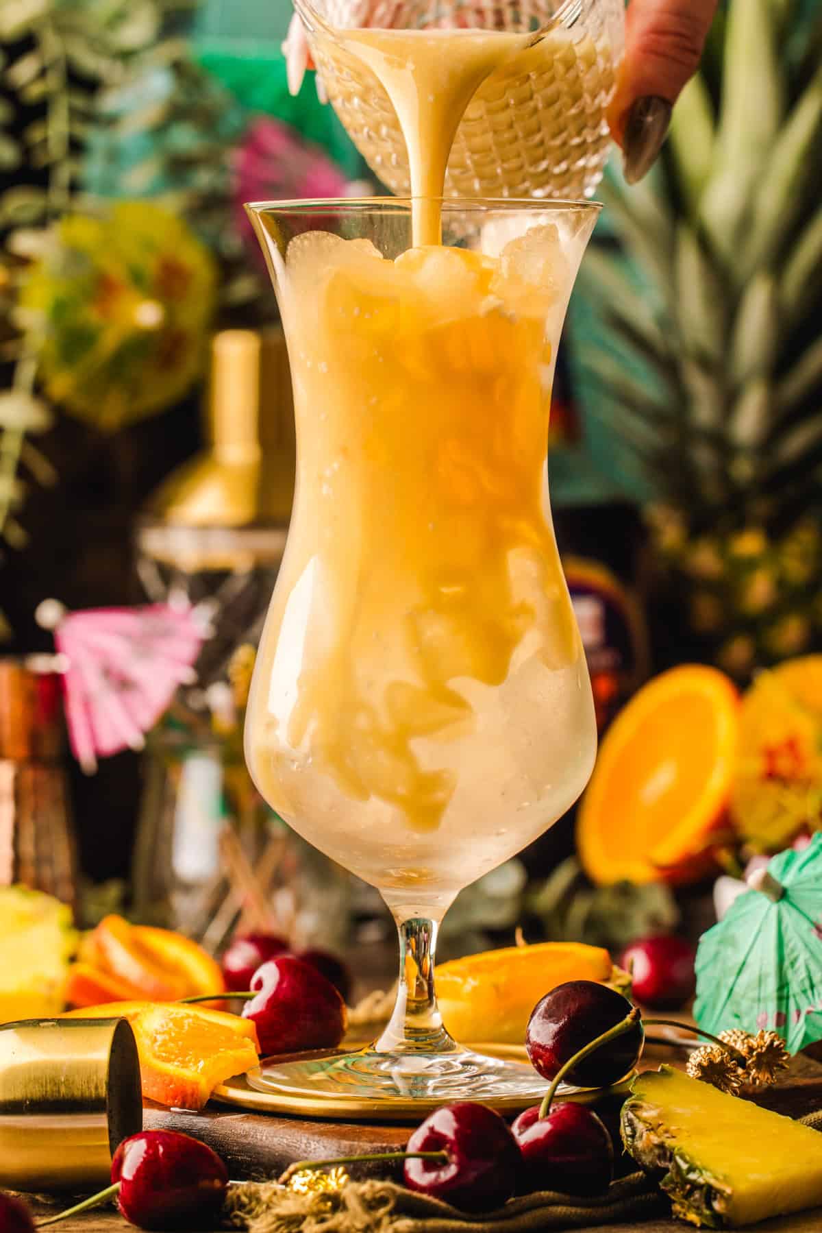 Painkiller Cocktail A creamy tropical drink is being poured over ice in a tall glass.