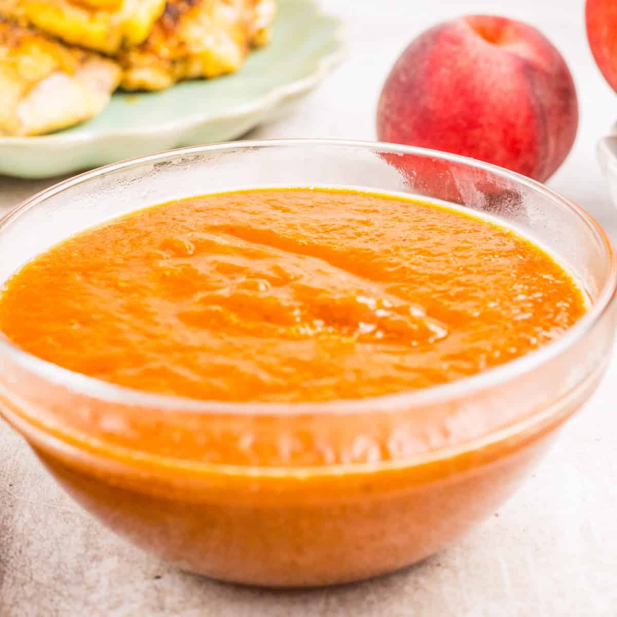A clear glass bowl filled with peach sauce sits on a light surface.