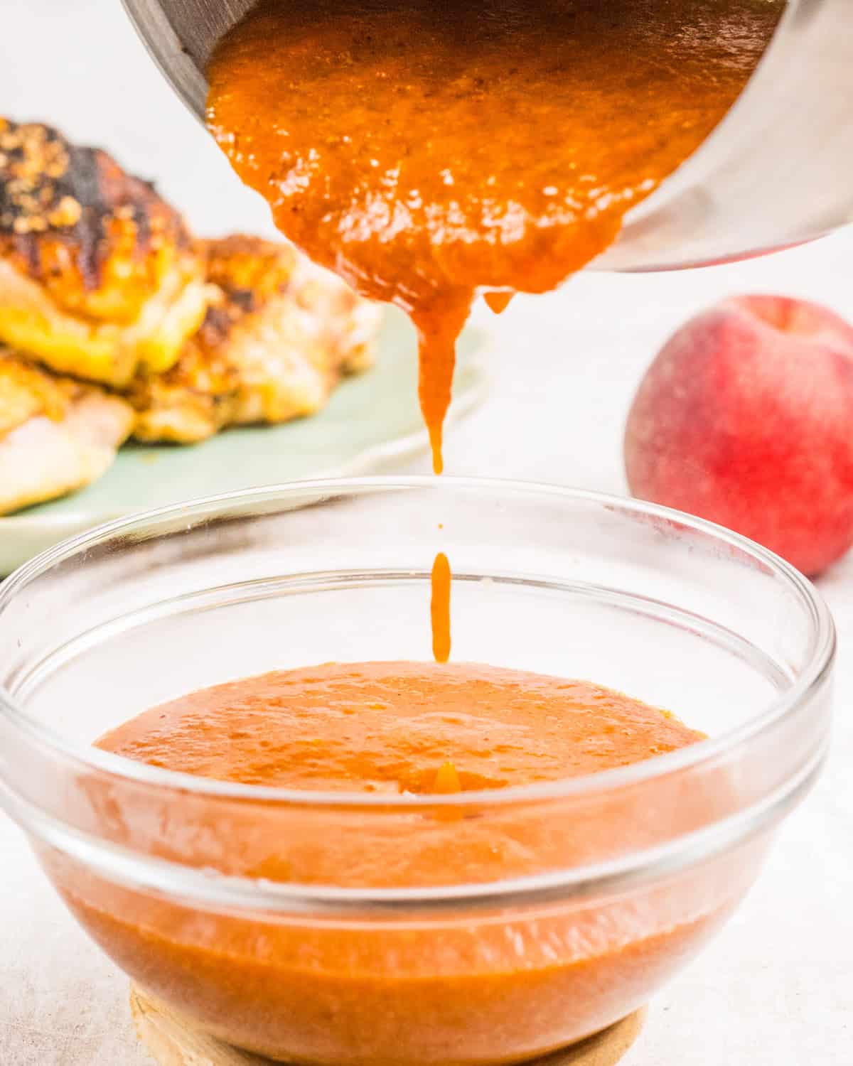 Peach sauce is being poured from a pot into a glass bowl. 