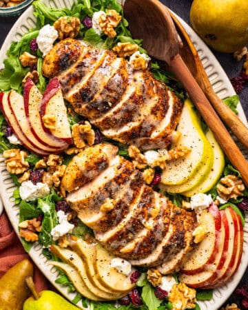 Sliced grilled chicken on a bed of greens with sliced apples, pears, walnuts, cranberries, and crumbled cheese.