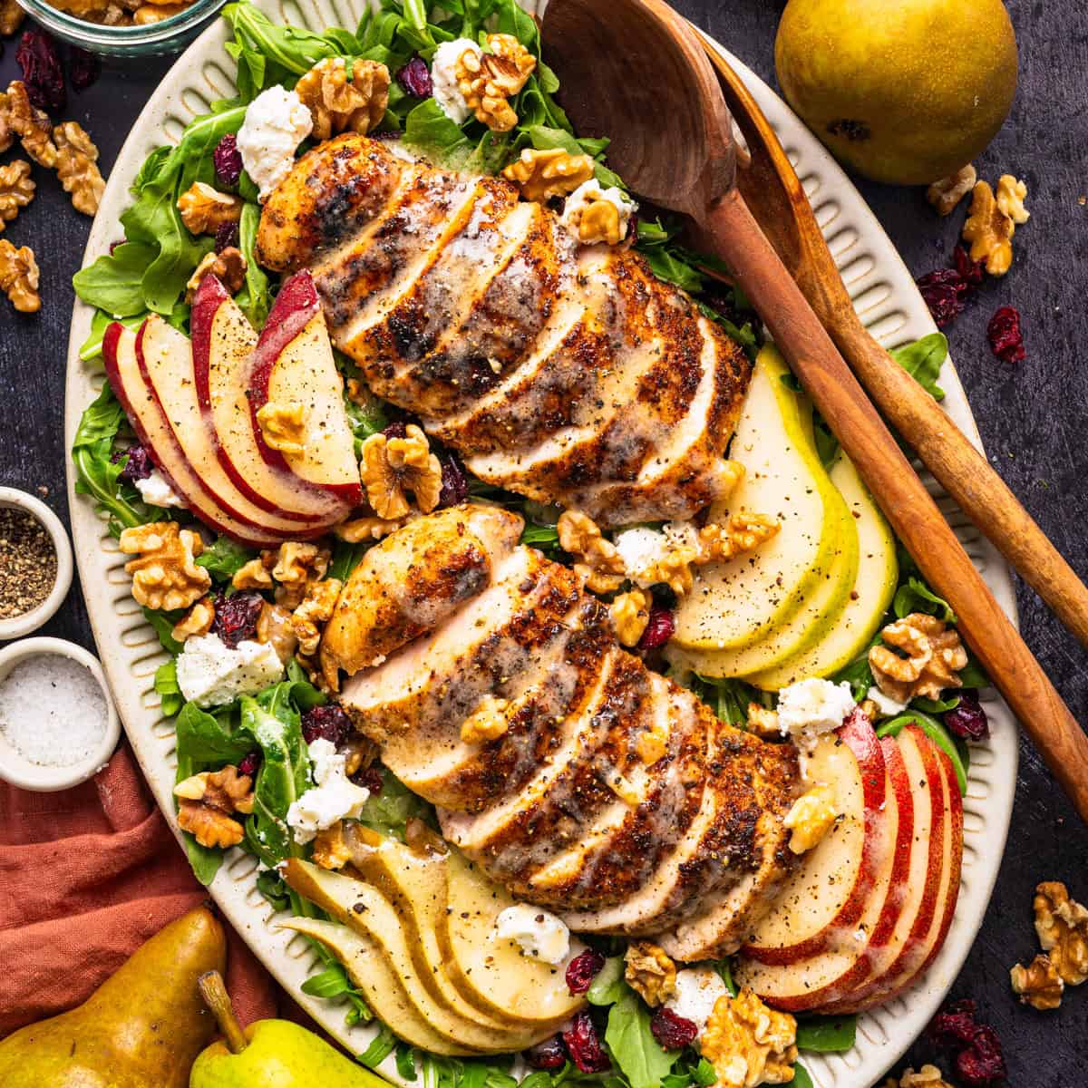 Sliced grilled chicken on a bed of greens with sliced apples, pears, walnuts, cranberries, and crumbled cheese.