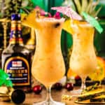 Two tropical cocktails in hurricane glasses with fruit garnishes and paper umbrellas.