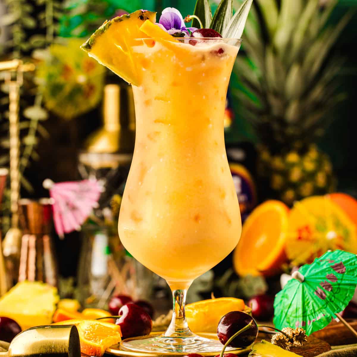 A tropical cocktail in a curved glass, garnished with a pineapple slice, cherry, and edible flower.