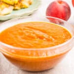 A clear glass bowl filled with thick orange peach sauce sits on a light surface.