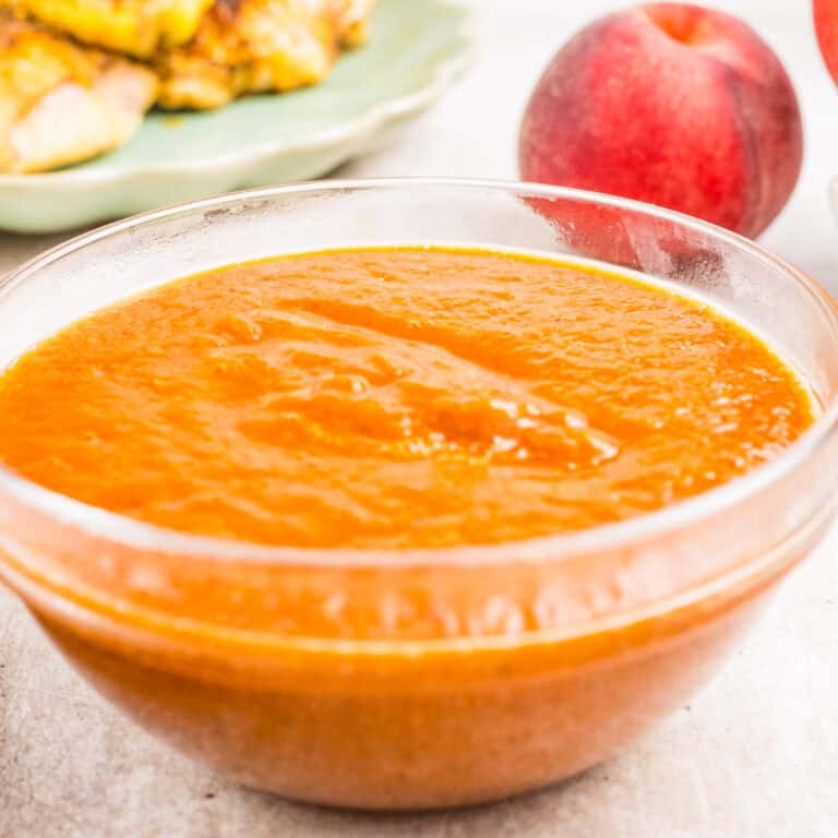 A clear glass bowl filled with thick orange peach sauce sits on a light surface.