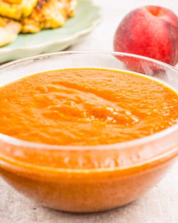 A clear glass bowl filled with thick peach sauce sits on a light surface.