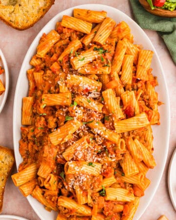 Oval platter of rigatoni pasta in a tomato-based meat sauce, topped with grated cheese.