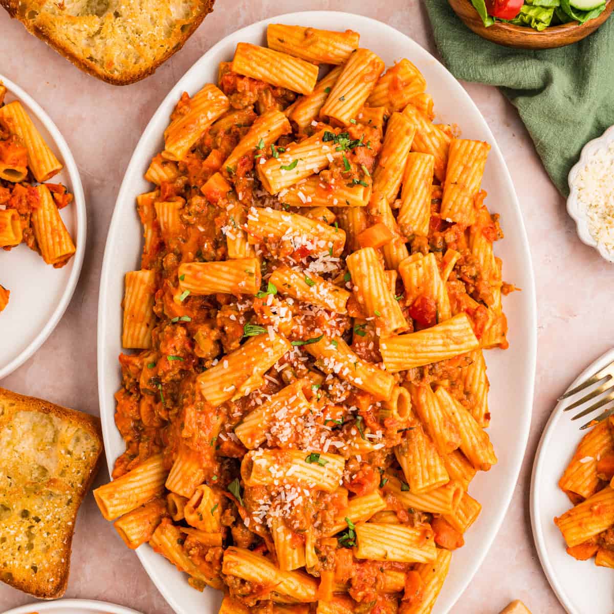 Oval platter of rigatoni pasta in a tomato-based meat sauce, topped with grated cheese.