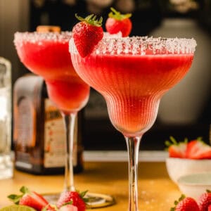 Two strawberry margaritas in salt-rimmed glasses, each garnished with a whole strawberry.
