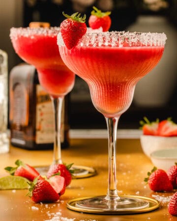 Two strawberry margaritas in salt-rimmed glasses, garnished with fresh strawberries.