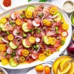 A platter of colorful tuna topped with sliced cucumbers, radishes, kumquats, capers, onions, and chili peppers.