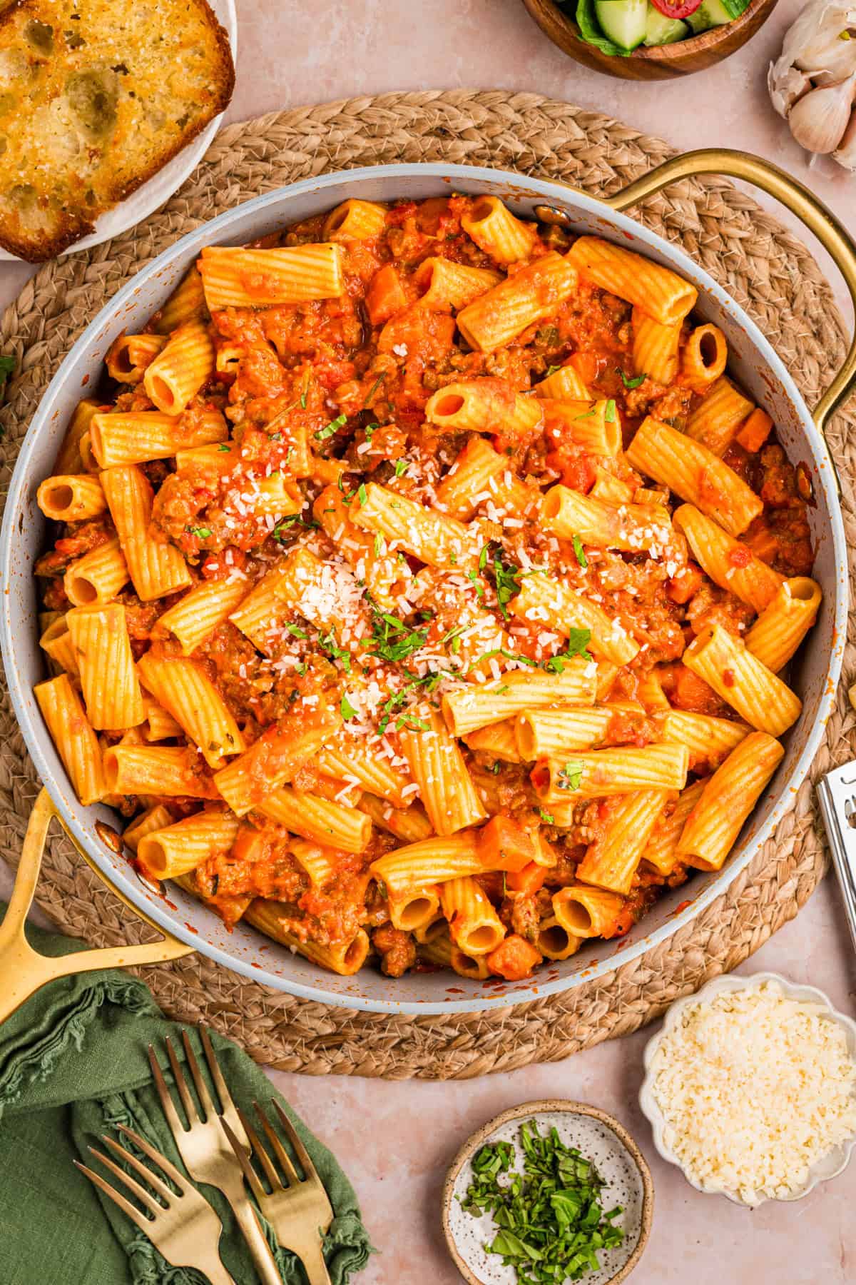 Large skillet filled with rigatoni pasta in a rich tomato sauce, topped with grated cheese and chopped herbs.