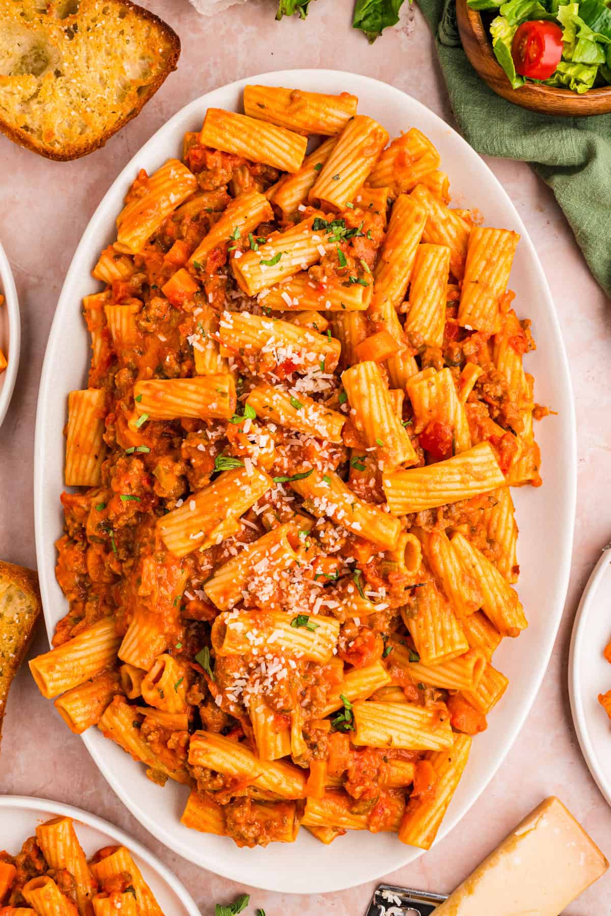 Sausage Ragu A white oval dish filled with rigatoni pasta in tomato sauce, topped with grated cheese and herbs.