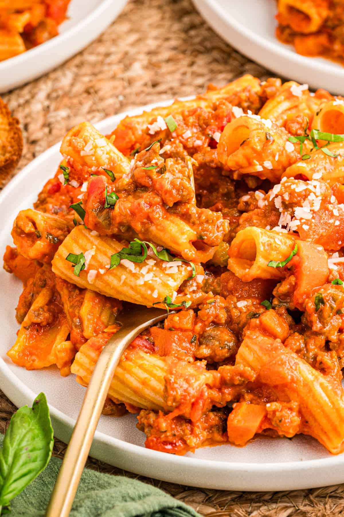 Sausage Ragu A plate of rigatoni pasta topped with a chunky tomato meat sauce, garnished with grated cheese and herbs.