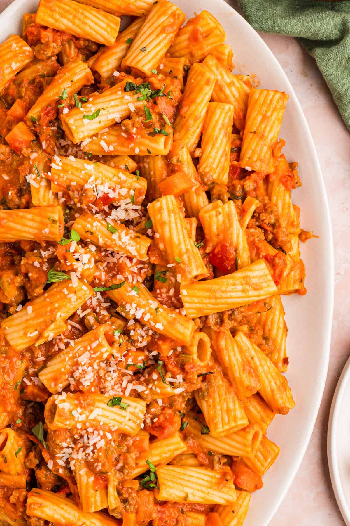 Sausage Ragu A close-up of rigatoni pasta with a chunky tomato and meat sauce, garnished with grated cheese and chopped herbs.