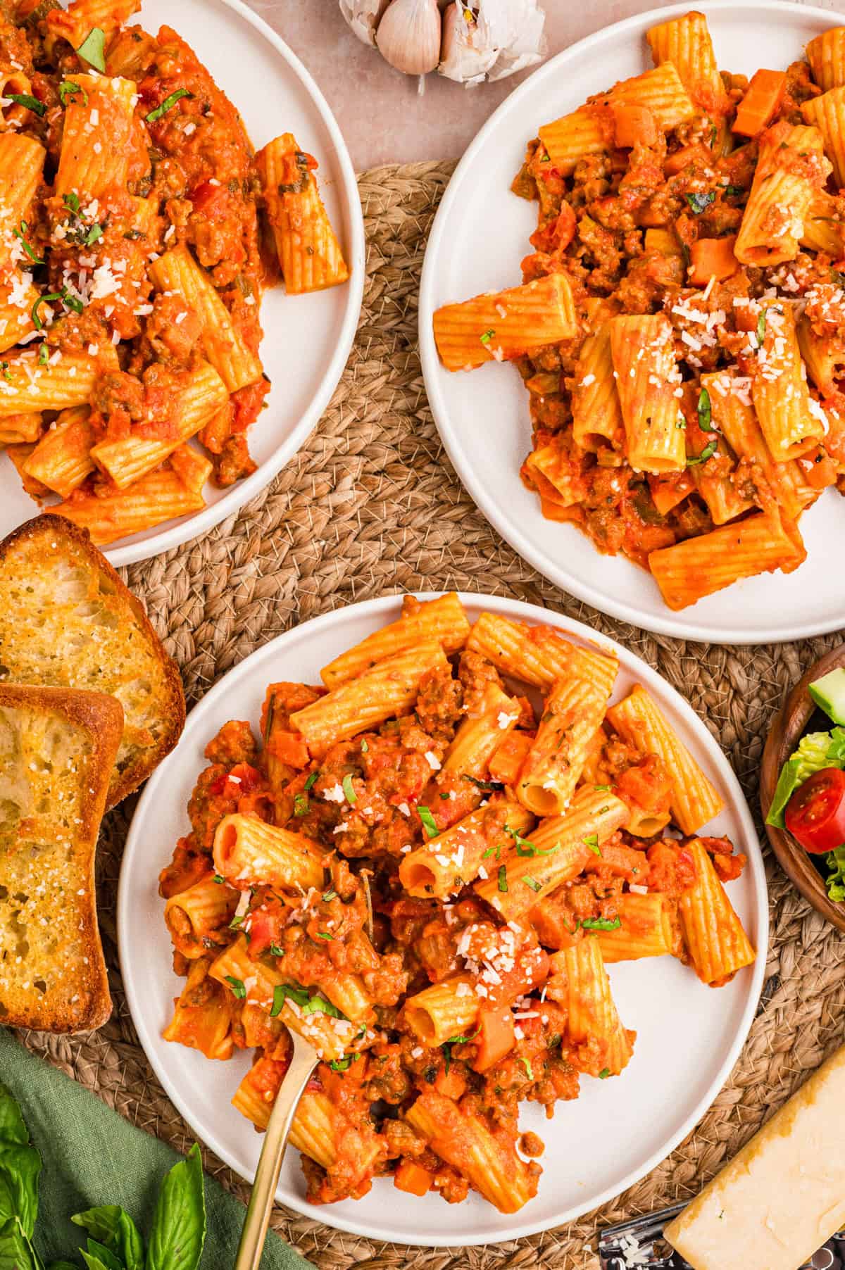 Sausage Ragu Three plates of rigatoni pasta with tomato sauce, ground meat, and vegetables, garnished with grated cheese.