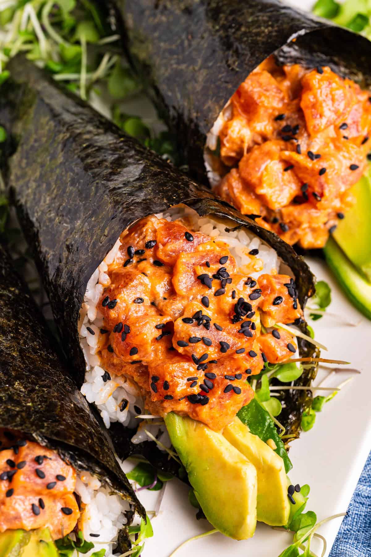 Spicy Tuna Hand Rolls Close-up of hand-rolled sushi cones filled with spicy tuna, white rice, avocado slices, and topped with black sesame seeds, wrapped in nori seaweed.