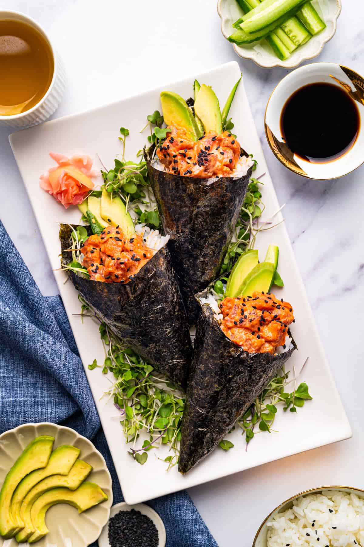 Spicy Tuna Hand Rolls Three sushi hand rolls filled with spicy tuna, avocado, and rice are arranged on microgreens.