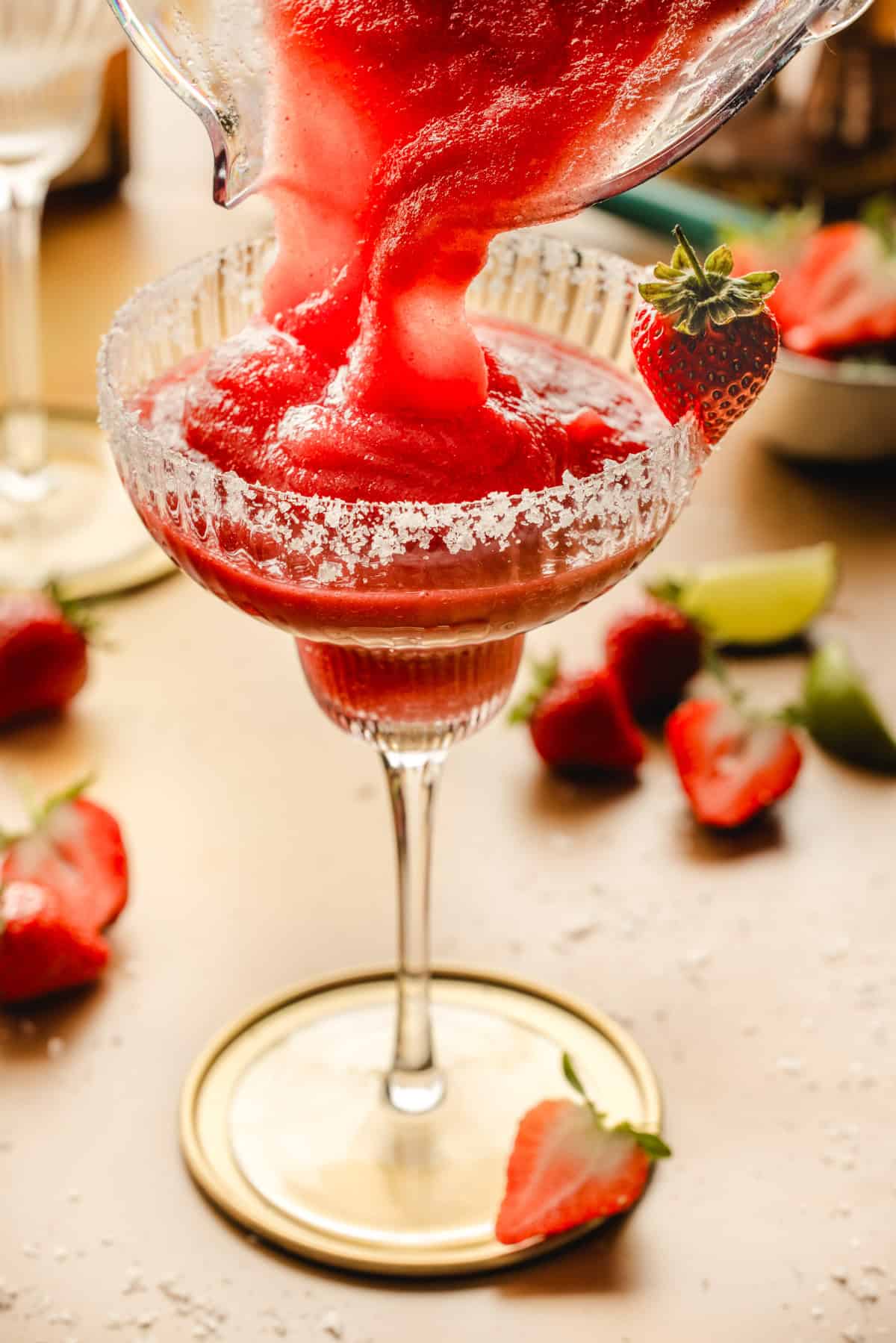 Strawberry Margarita A blended strawberry margarita is being poured into a rimmed glass, garnished with a fresh strawberry.