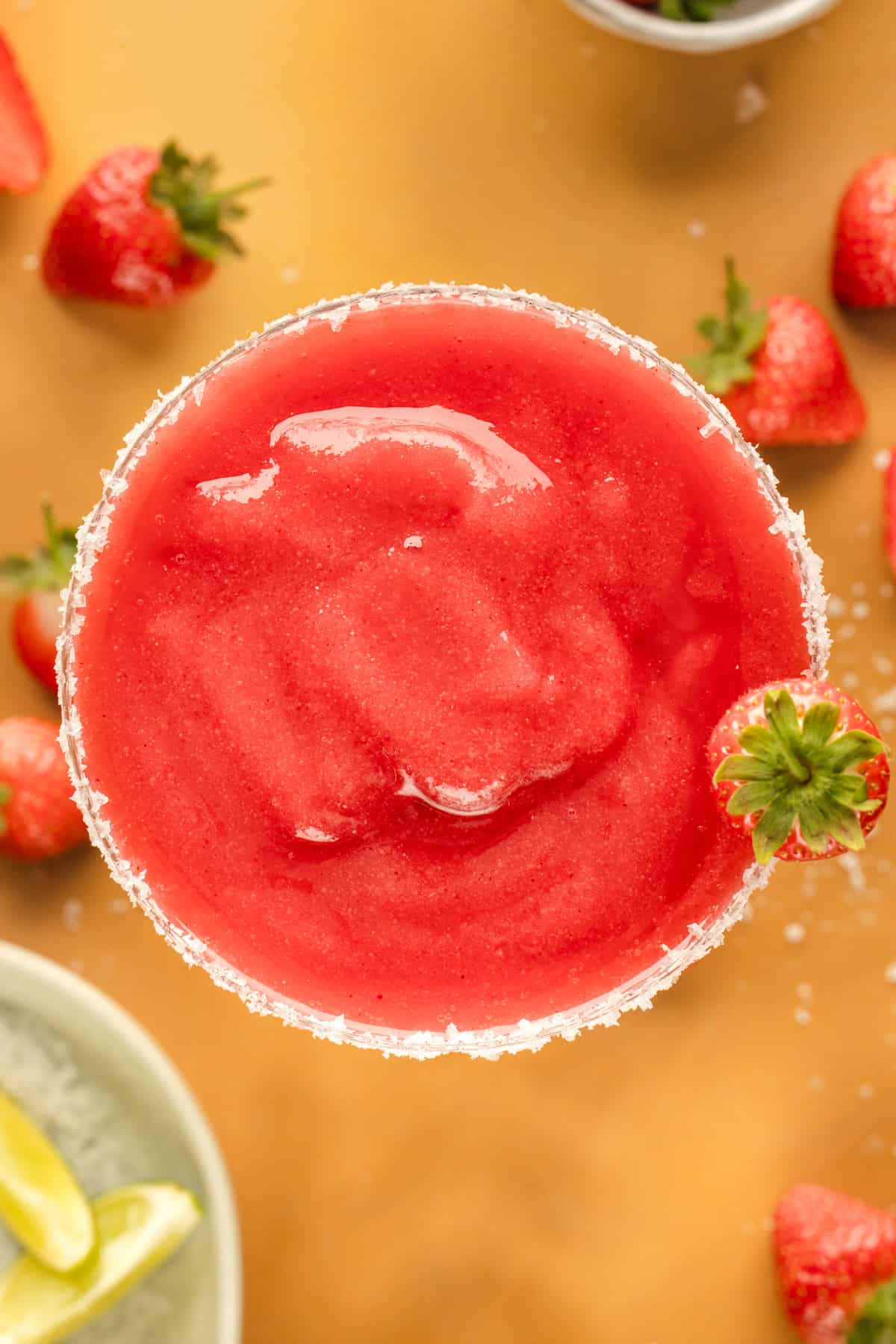 Strawberry Margarita A top-down view of a bright red frozen strawberry margarita in a glass with a salted rim, garnished with a fresh strawberry.