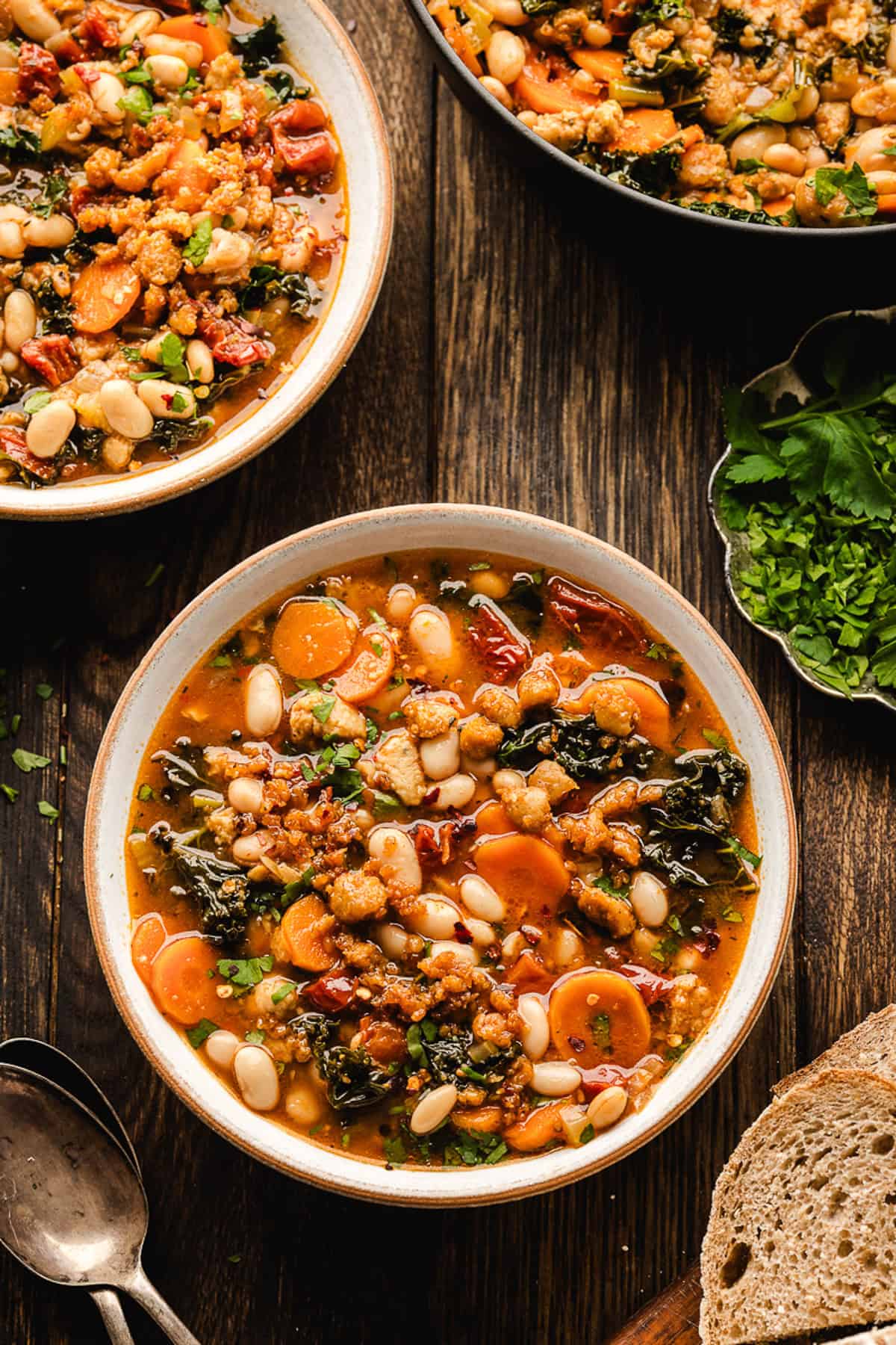 Tuscan White Bean Soup A bowl of hearty Tuscan White Bean Soup with carrots, greens, white beans, and herbs sits on a rustic wooden table.