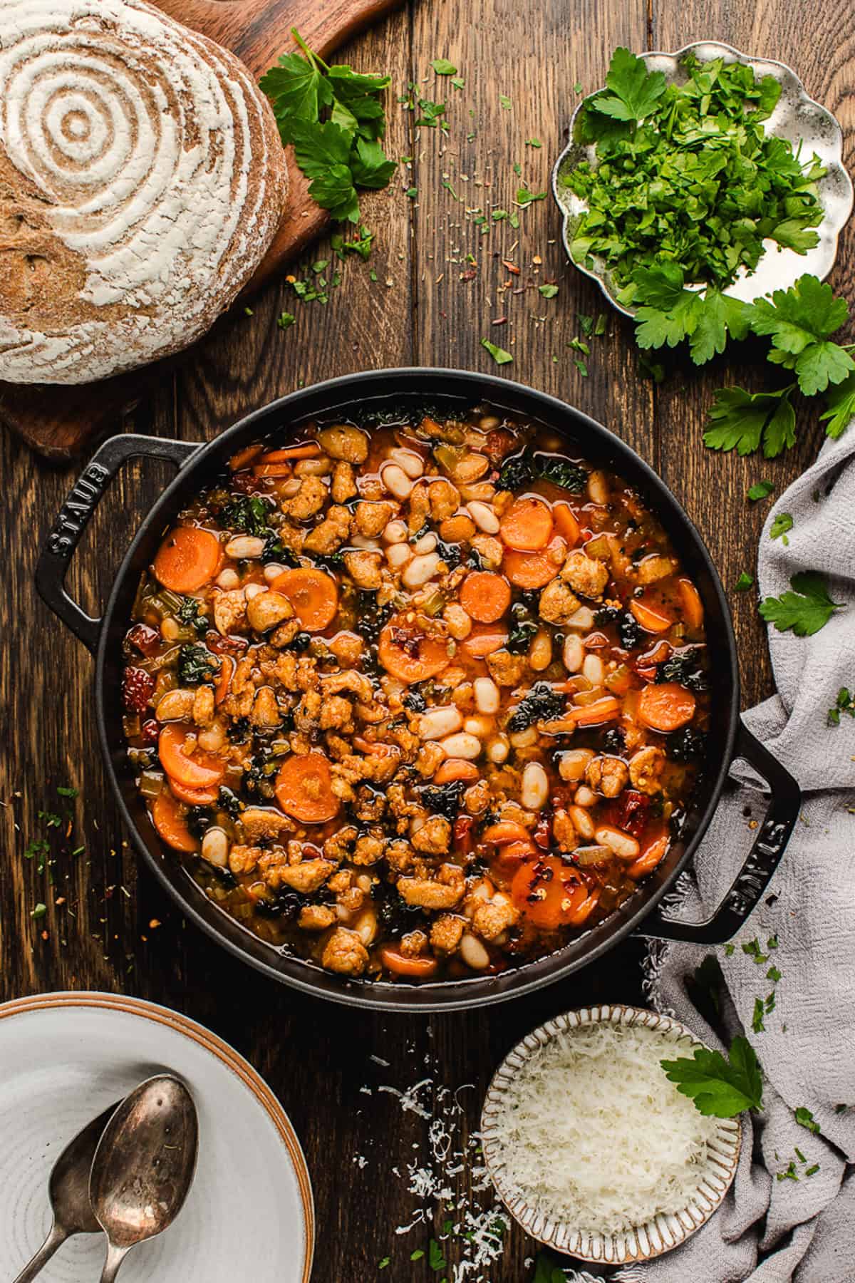 Tuscan White Bean Soup A pot of Tuscan White Bean Soup with beans, carrots, greens, and sausage on a wooden table.