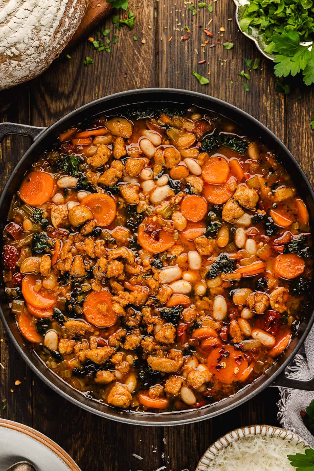 Tuscan White Bean Soup A pot of Tuscan White Bean Soup with carrots, white beans, kale, and crumbled sausage sits on a dark wooden table.