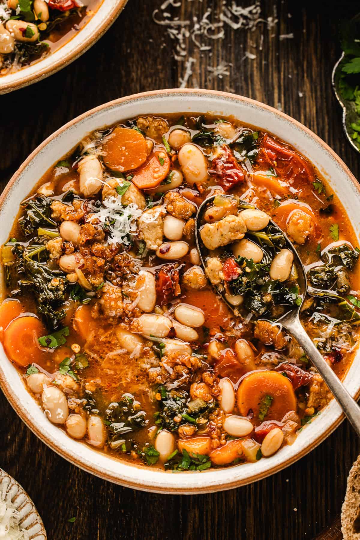Tuscan White Bean Soup A bowl of Tuscan White Bean Soup with white beans, kale, carrots, sun-dried tomatoes, and crumbled sausage, garnished with grated cheese and herbs.