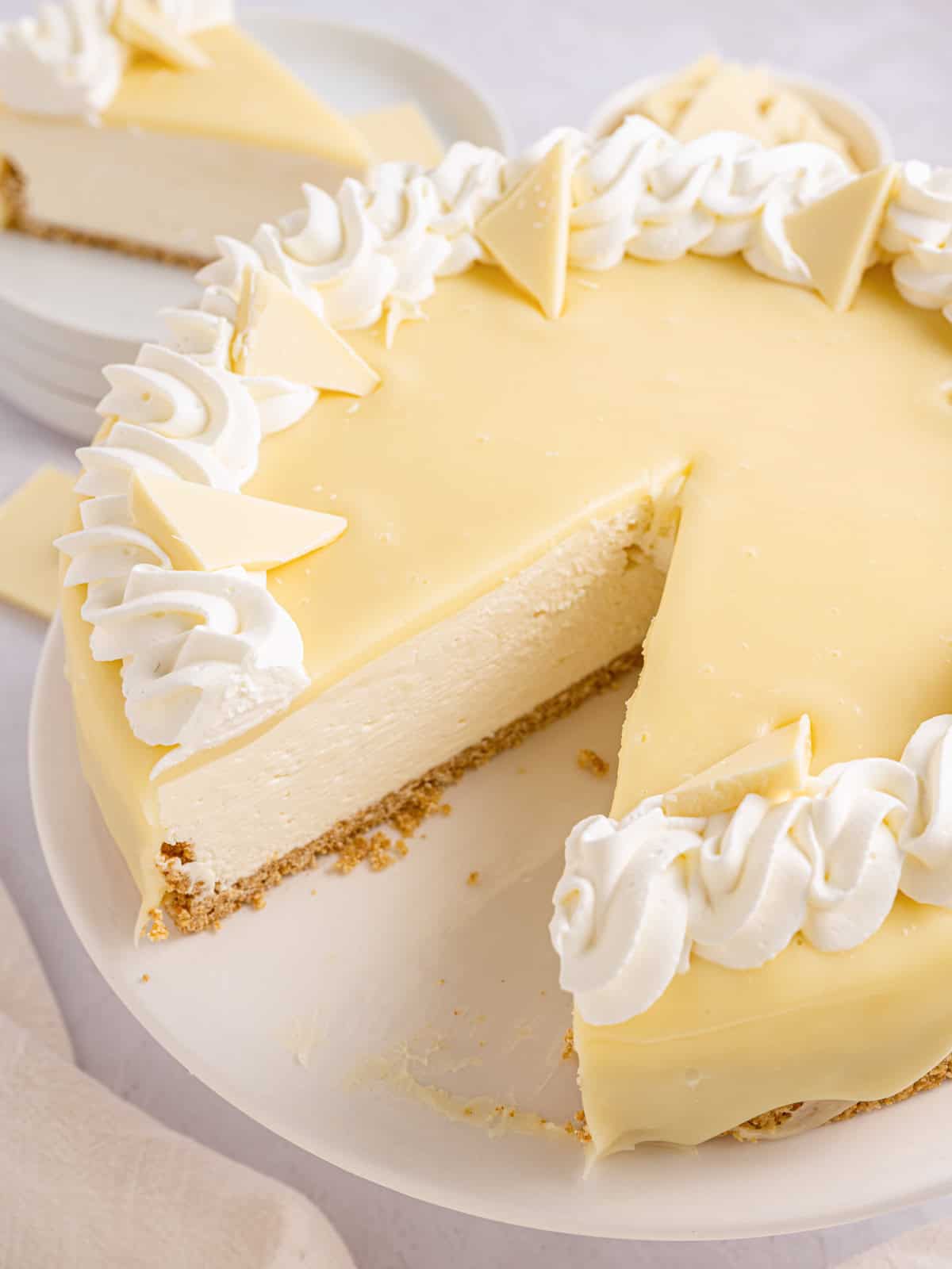 White Chocolate Cheesecake A creamy white cheesecake topped with whipped cream and white chocolate pieces, with one slice cut and partially removed.
