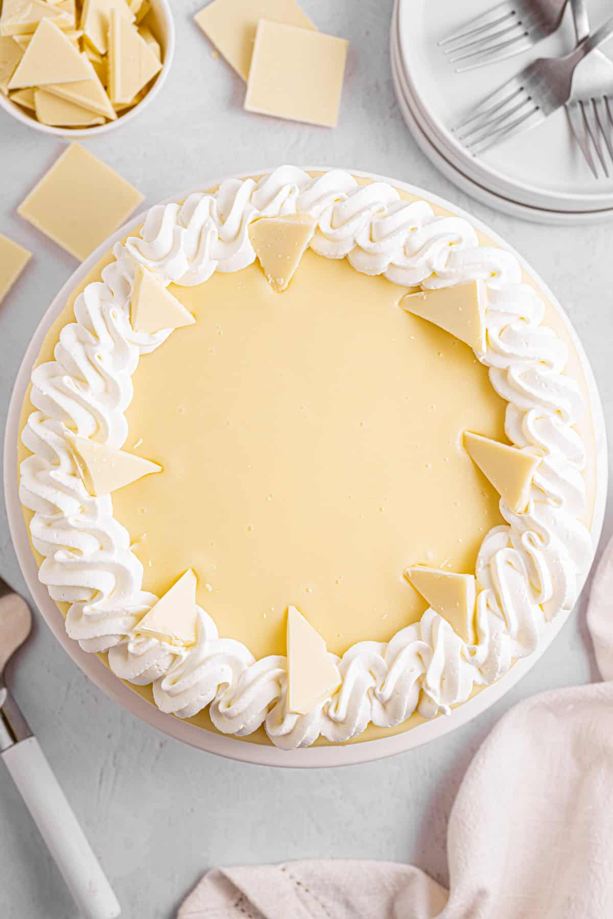 White Chocolate Cheesecake A round white chocolate cheesecake topped with whipped cream swirls and white chocolate triangles.