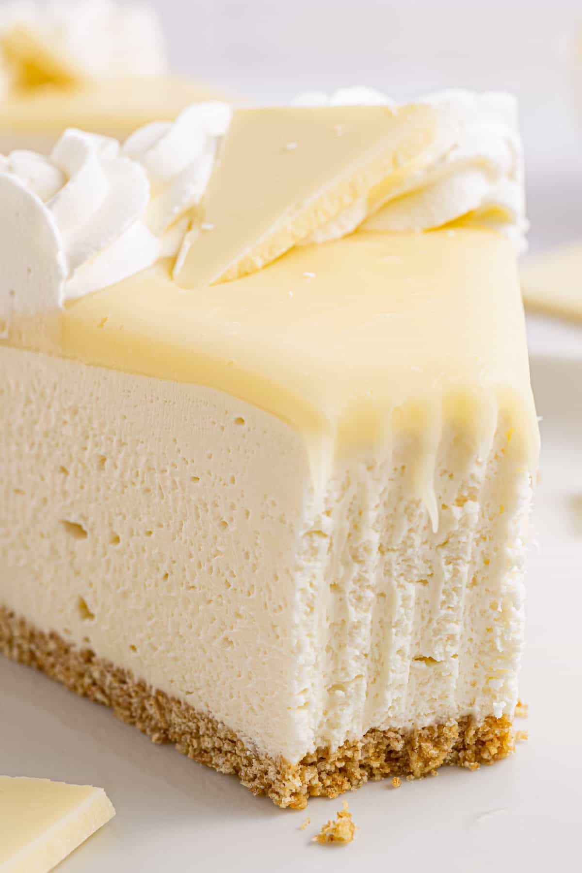 White Chocolate Cheesecake A slice of creamy white cheesecake with a graham cracker crust, topped with white chocolate, whipped cream, and a bite taken out of it.