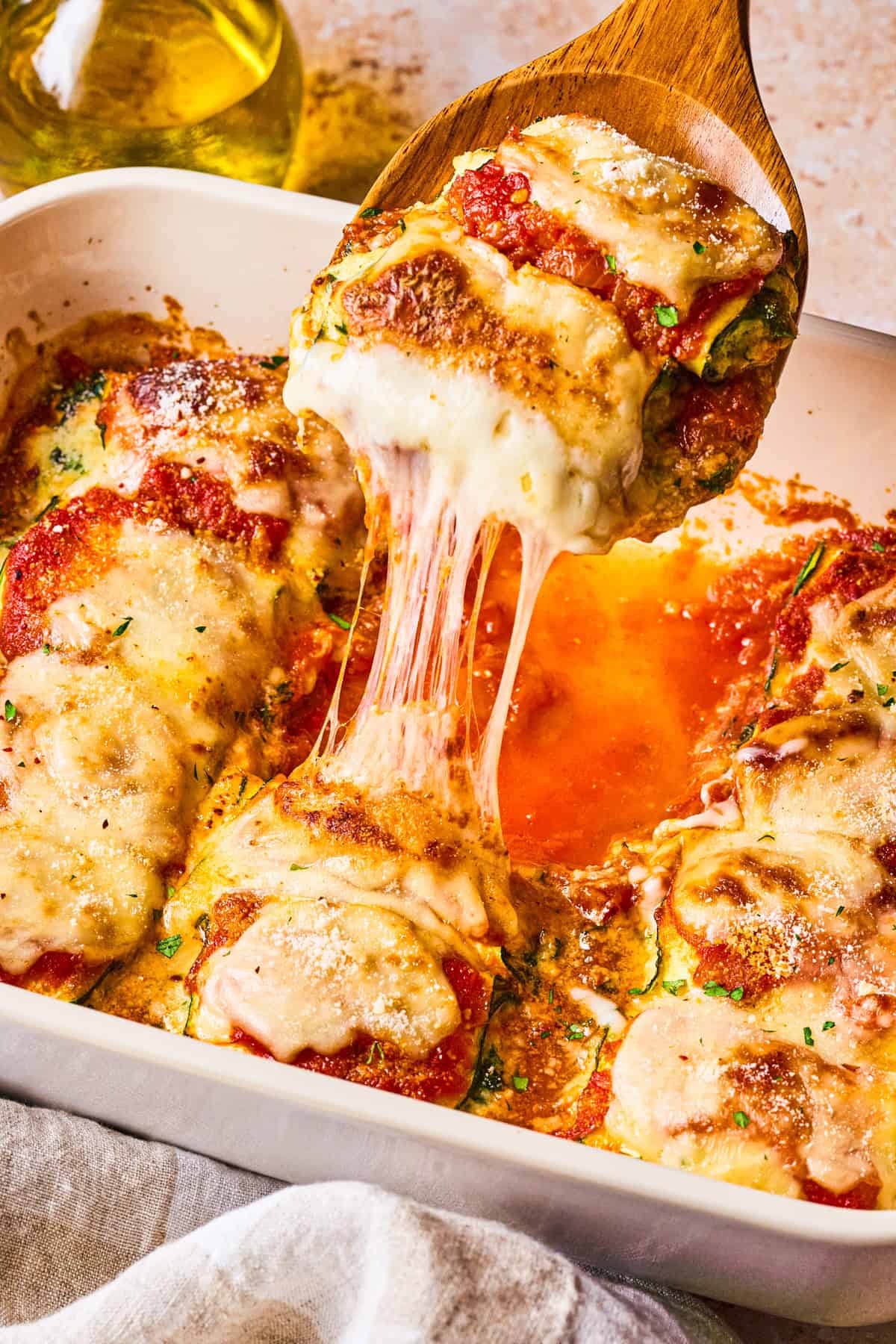 Zucchini Rollatini A wooden spoon lifts a cheesy, saucy baked zucchini slice from a casserole dish, showing melted cheese stretching.