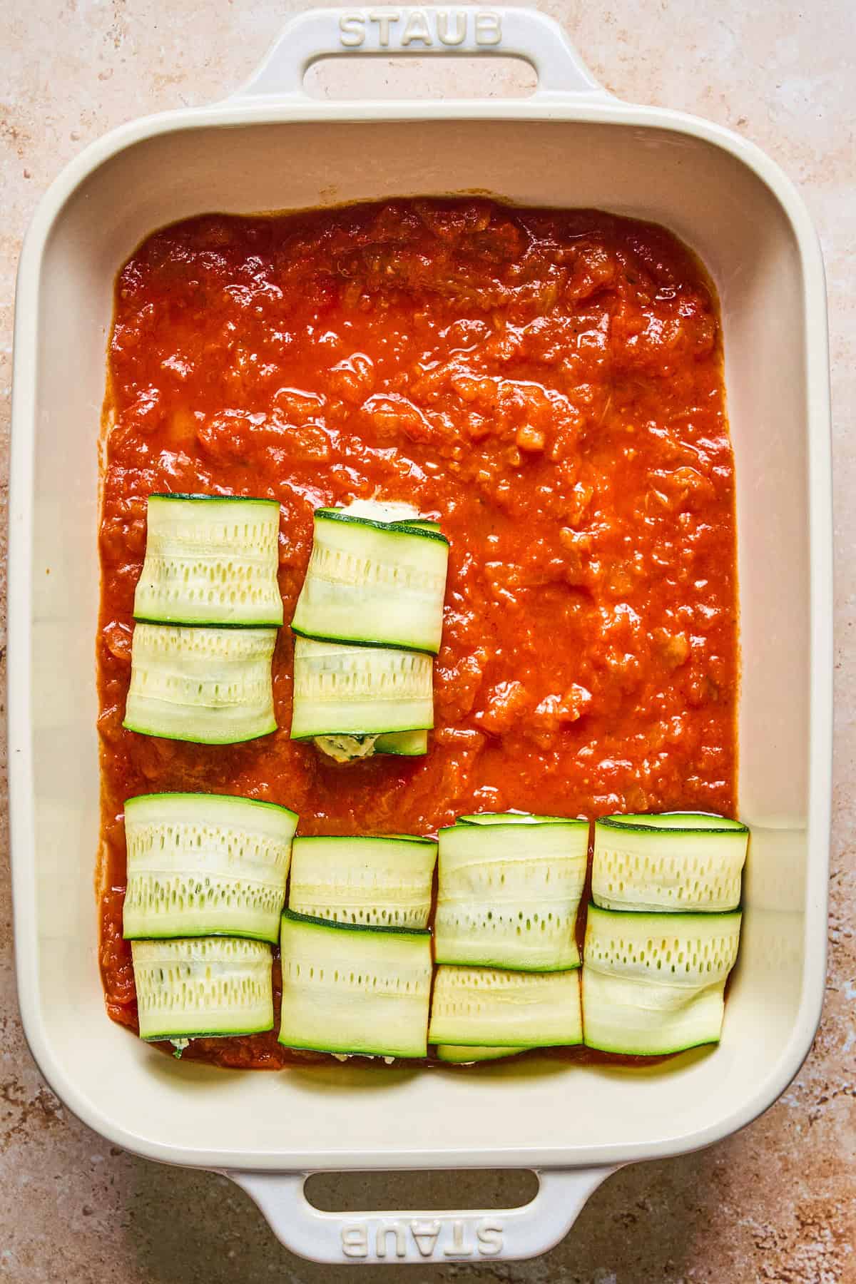 Zucchini Rollatini A baking dish with tomato sauce and zucchini roll-ups arranged on top.