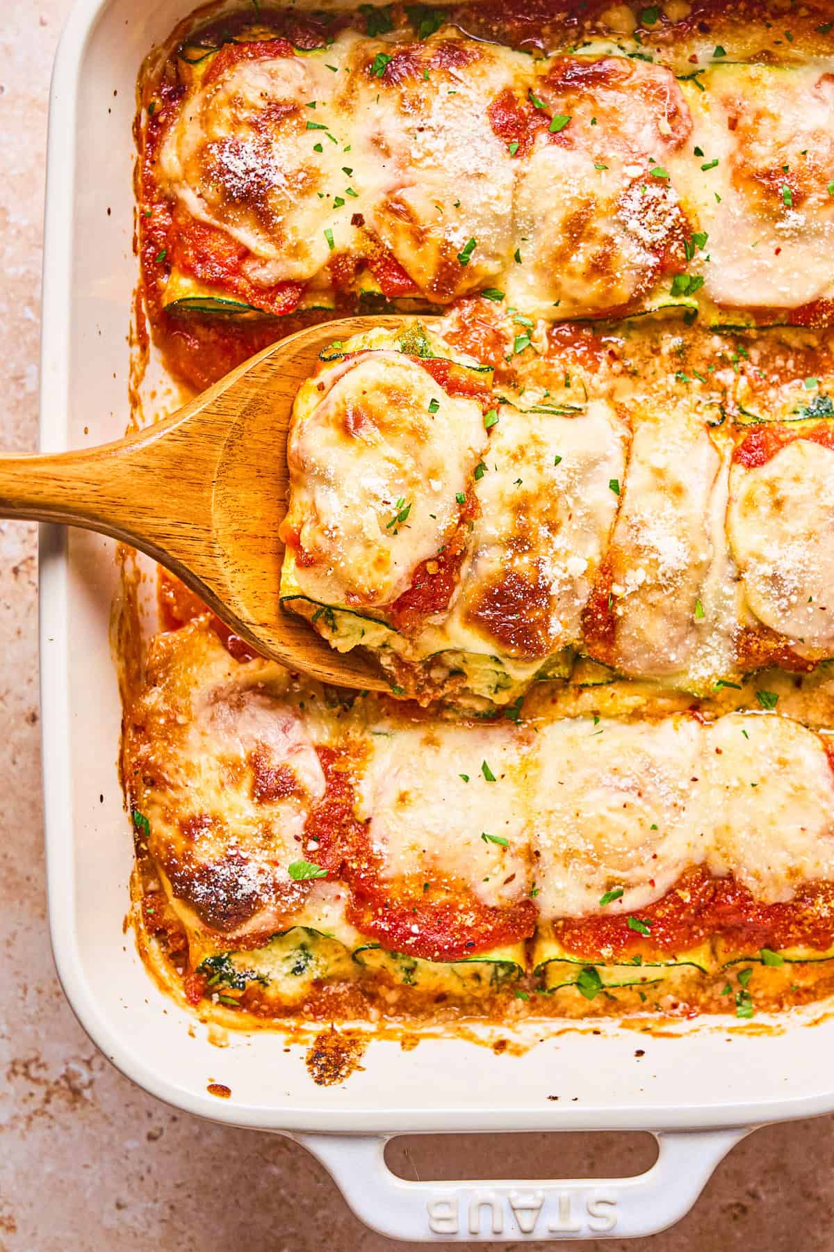 Zucchini Rollatini A wooden spatula lifts a cheesy, saucy zucchini slice from a white baking dish.
