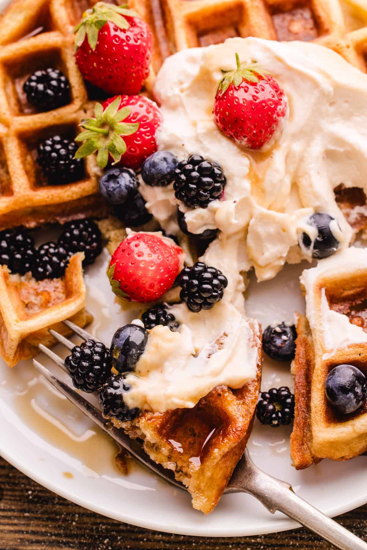 A plate of waffles topped with cream, strawberries, blackberries, blueberries, and syrup. 