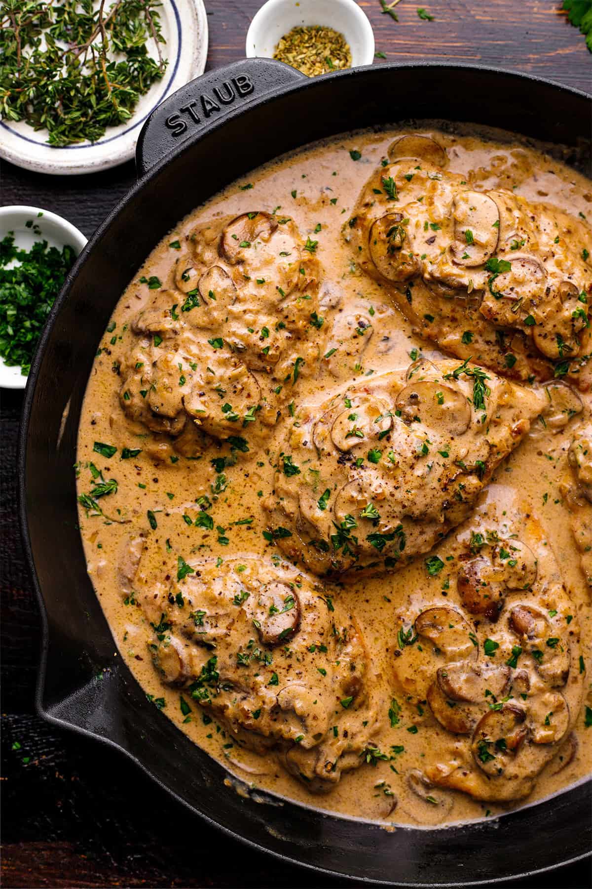 Chicken breasts simmering in a creamy mushroom sauce, garnished with chopped parsley, in a black cast iron skillet. 