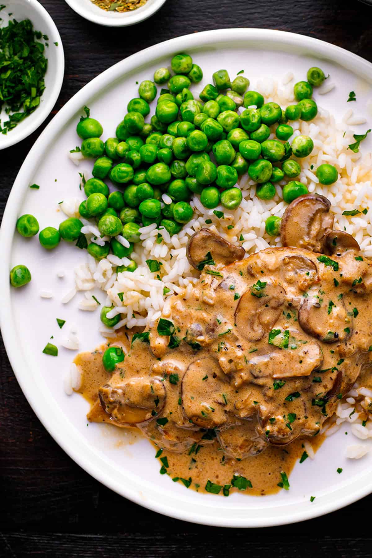 Chicken Marsala A white plate with cooked rice, green peas, and creamy mushroom stroganoff, garnished with chopped herbs.