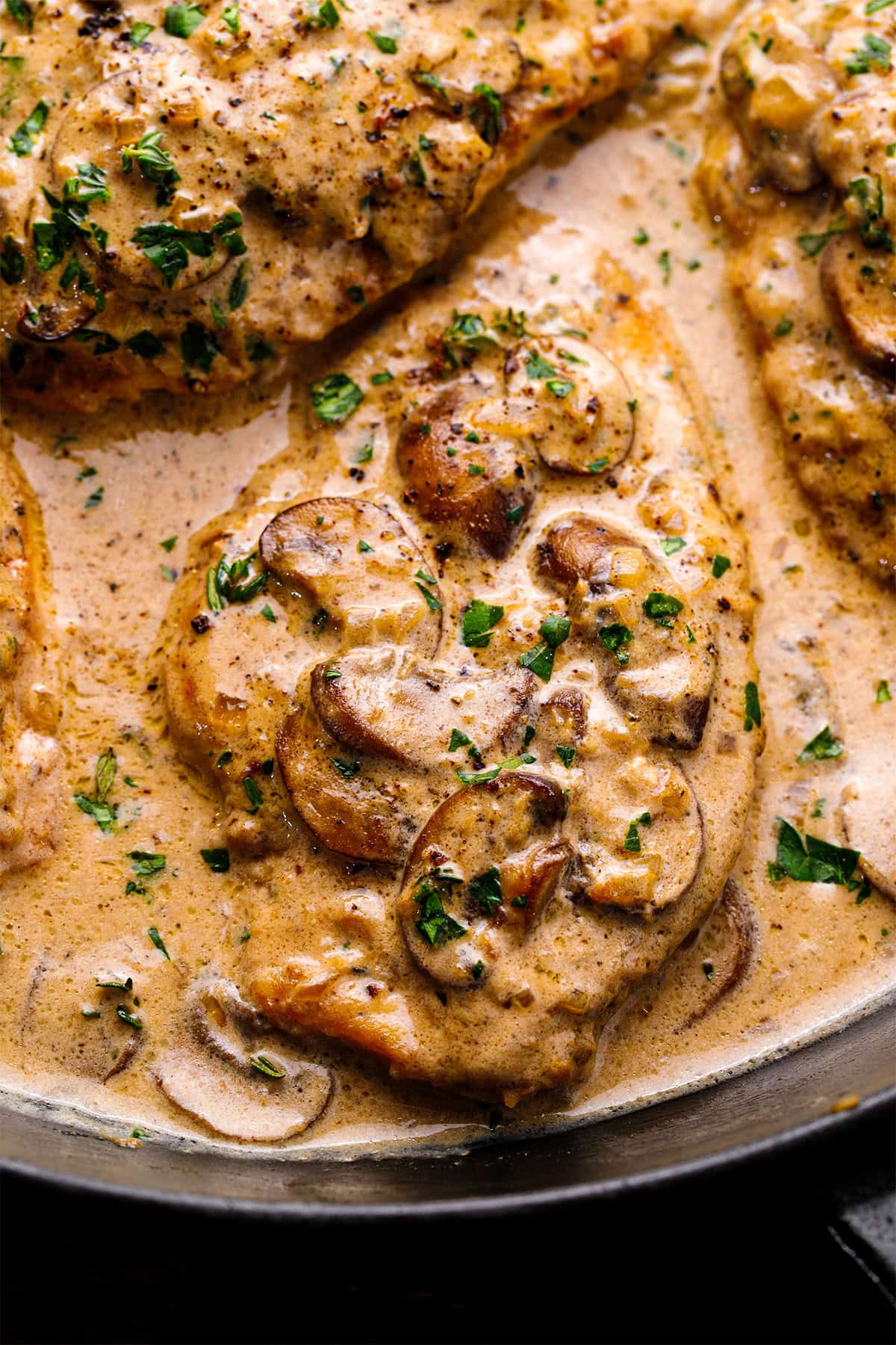 Chicken Marsala Chicken breasts in a creamy mushroom sauce, garnished with chopped parsley, cooking in a skillet.