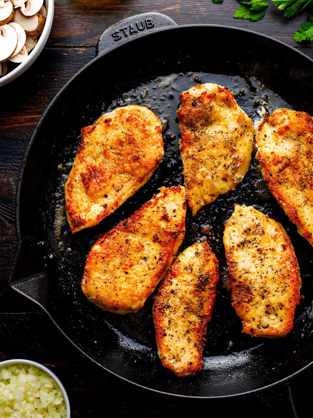 Chicken Marsala Six seasoned chicken breasts are shown searing in a black cast-iron skillet.