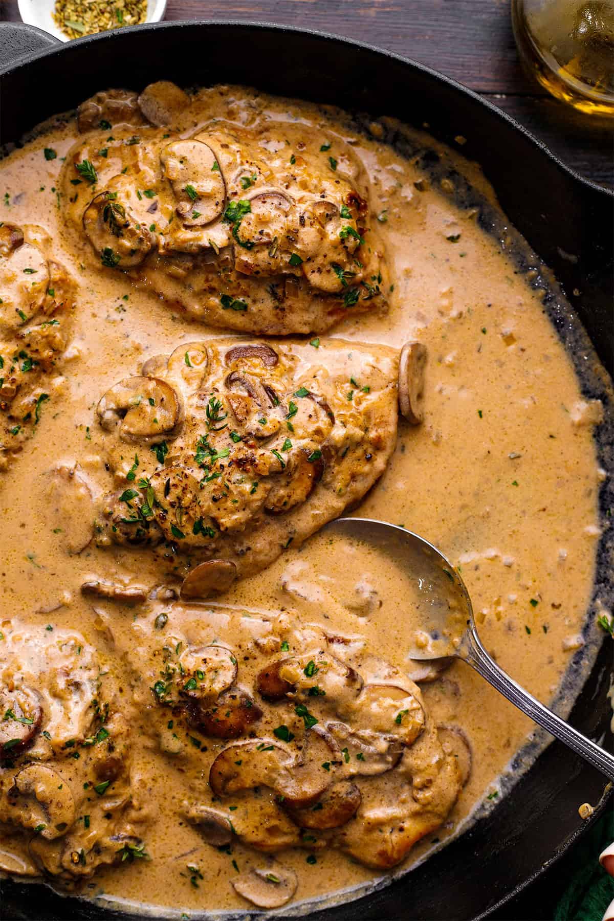 Chicken Marsala Chicken breasts in a creamy mushroom sauce, garnished with chopped herbs, served in a black skillet with a silver spoon resting in the sauce.