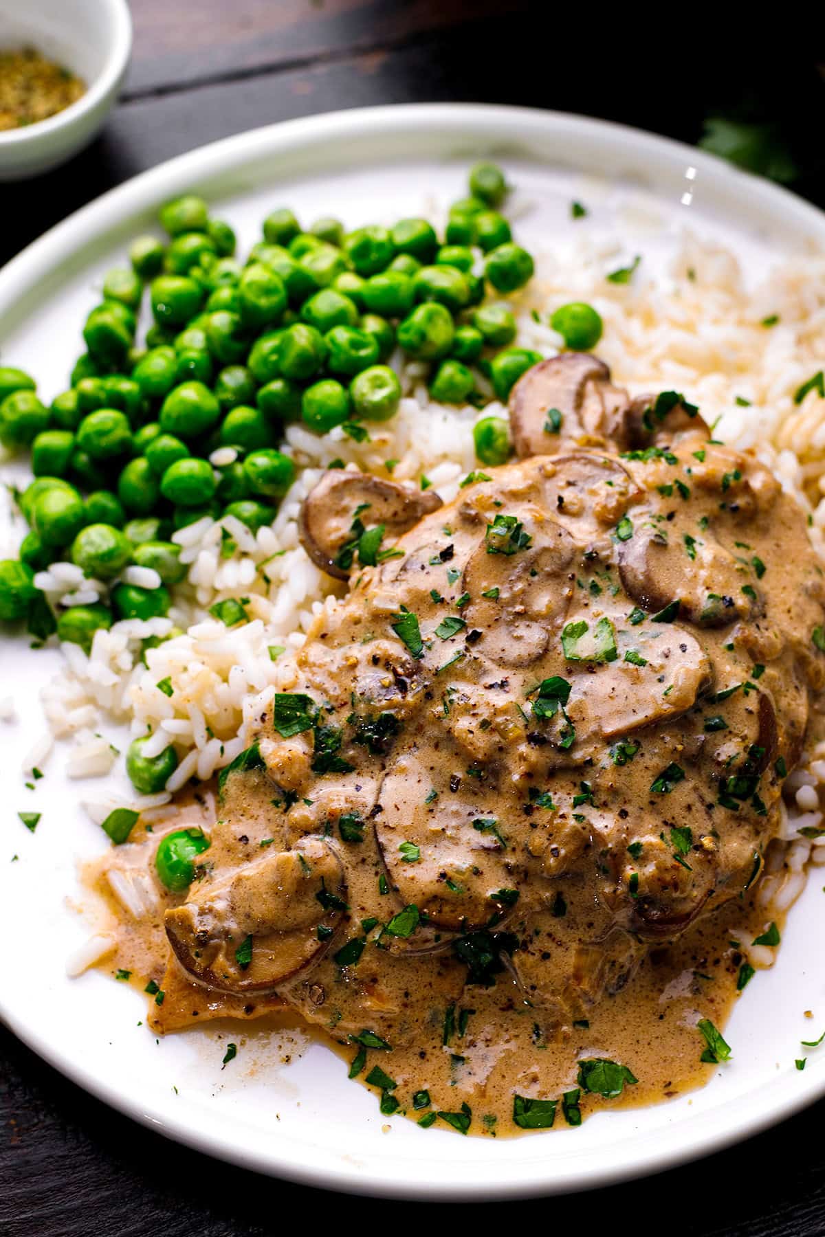 Chicken Marsala A plate with creamy mushroom sauce over meat, white rice, and green peas, garnished with chopped herbs.