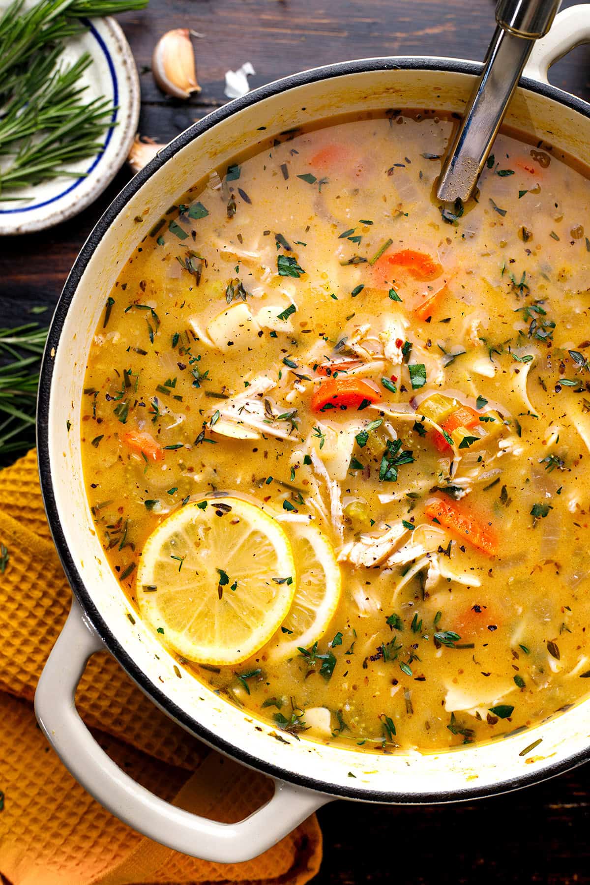 Chicken Noodle Soup A pot of chicken soup with shredded chicken, carrot slices, lemon rounds, herbs, and broth, with a ladle inside.