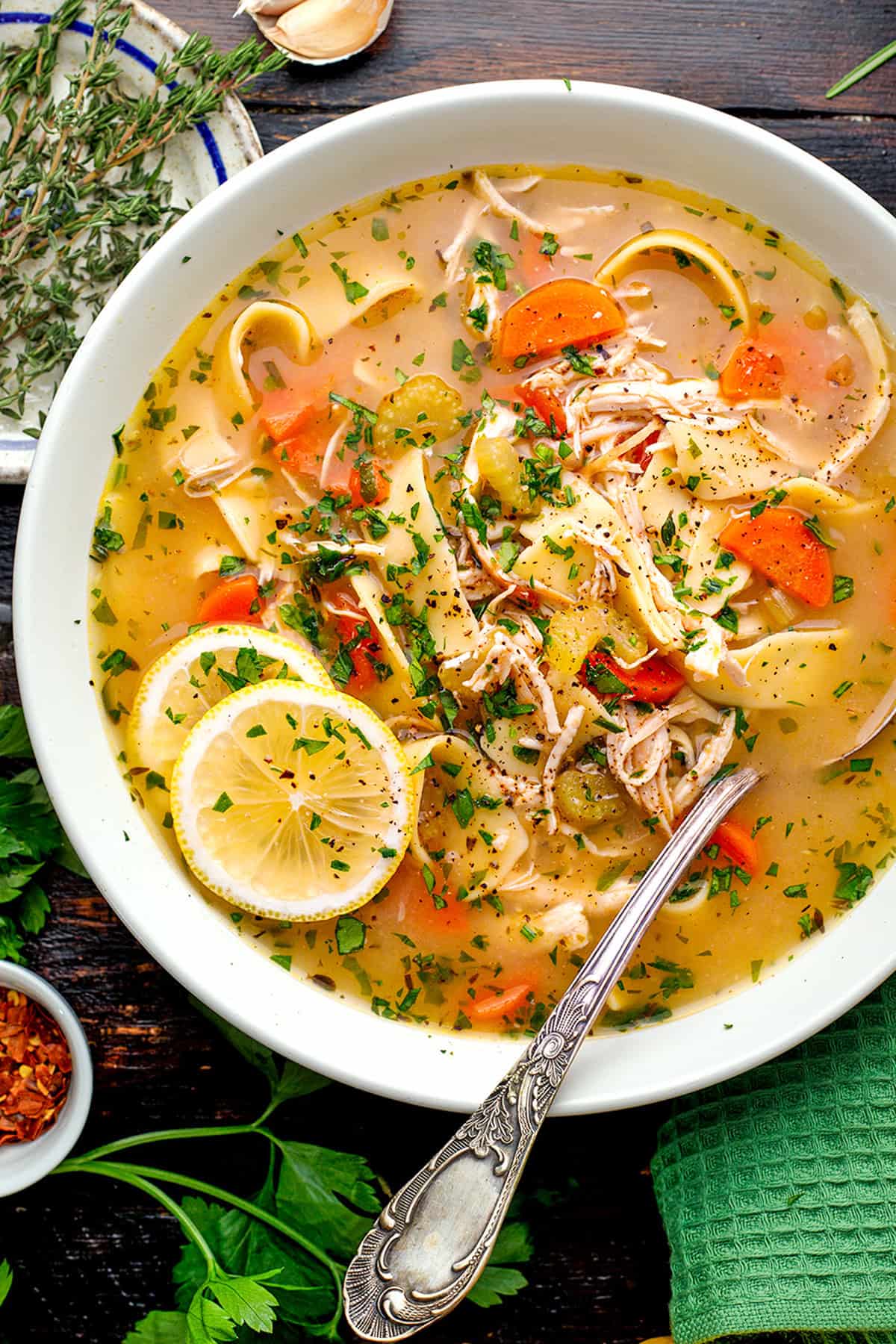 Chicken Noodle Soup A bowl of chicken noodle soup with carrots, celery, herbs, and lemon slices, garnished with parsley.