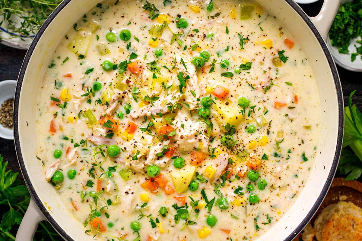Chicken Pot Pie Soup A creamy chicken and vegetable soup in a pot, filled with peas, carrots, corn, potatoes, and herbs, garnished with cracked pepper and fresh thyme.