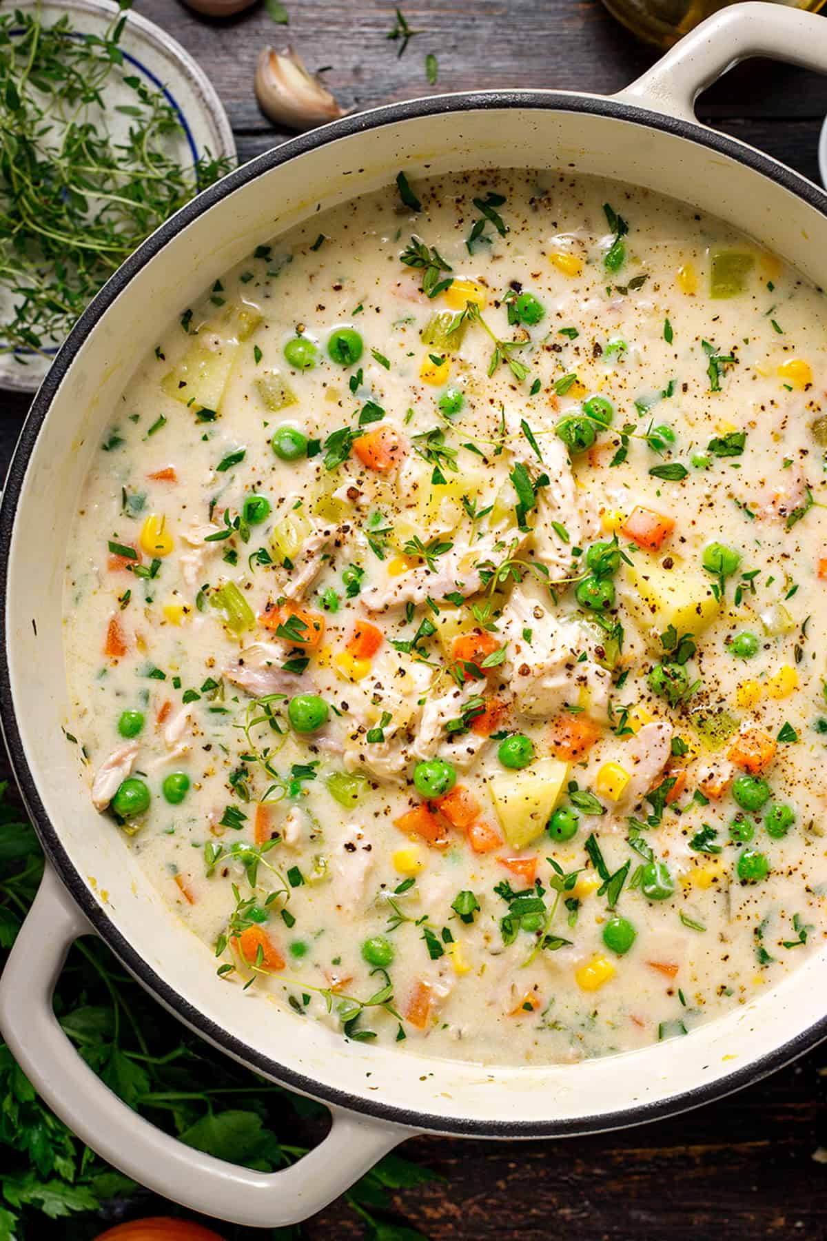 Chicken Pot Pie Soup A pot of creamy chicken and vegetable soup garnished with fresh herbs, containing peas, carrots, corn, potatoes, and shredded chicken.