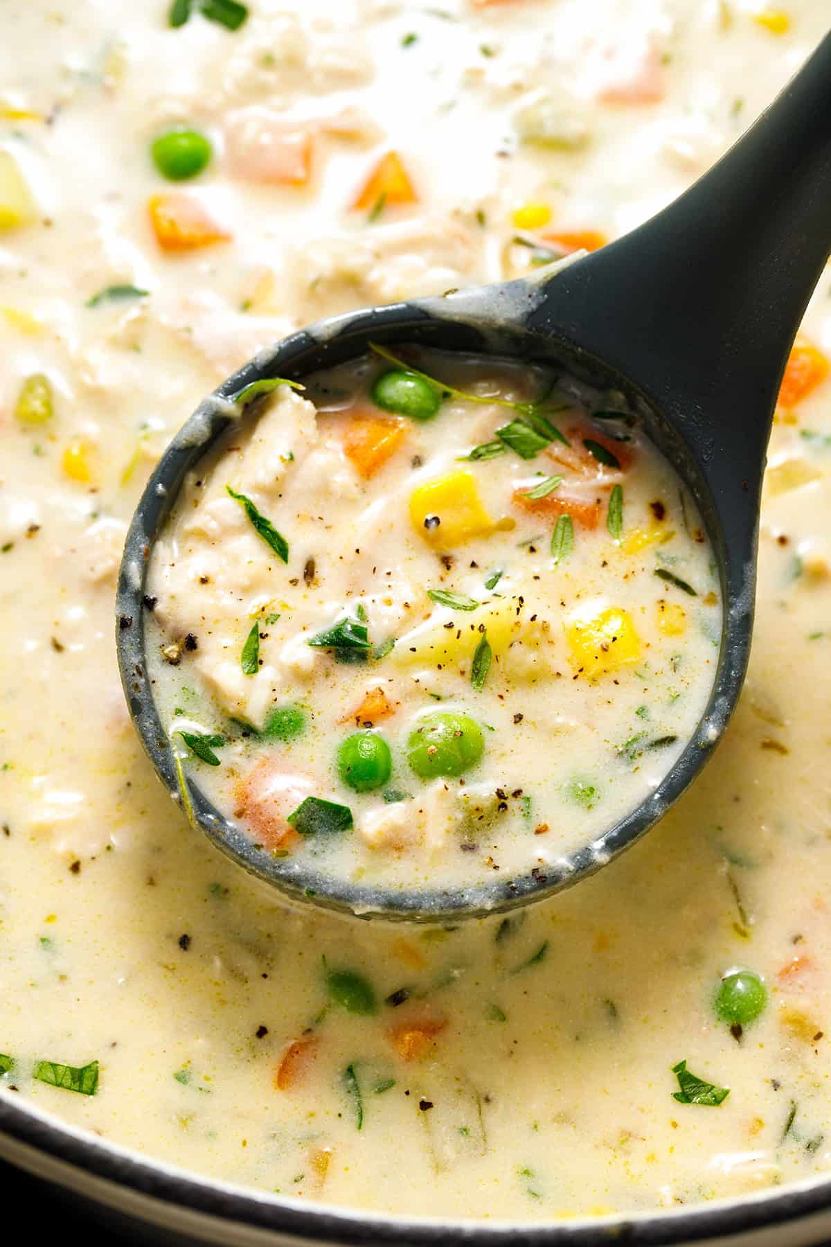 Chicken Pot Pie Soup A black ladle scoops creamy soup with chicken, peas, corn, carrots, and herbs from a pot.